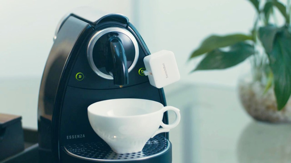 コーヒーメーカーのボタンに取り付けた SwitchBot ボット。白い小型の指ロボットがスイッチを物理的に押す
